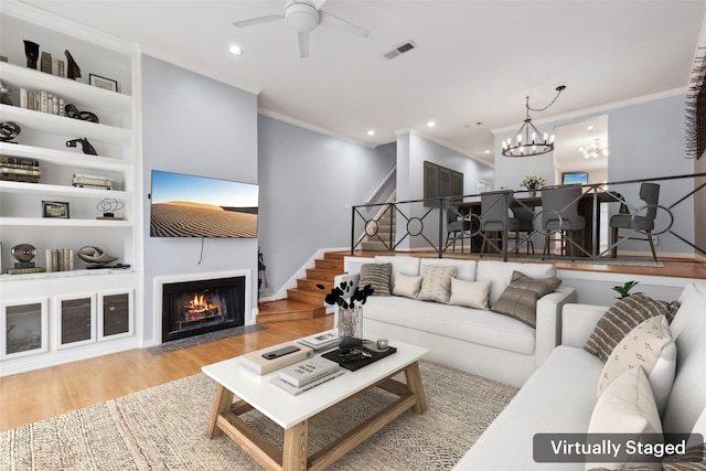 living room with light hardwood / wood-style floors, built in shelves, crown molding, and ceiling fan with notable chandelier