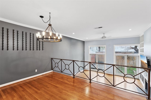 empty room featuring ceiling fan with notable chandelier, crown molding, and hardwood / wood-style floors