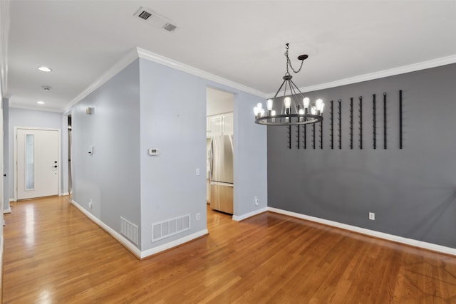 unfurnished dining area featuring an inviting chandelier, crown molding, and hardwood / wood-style floors