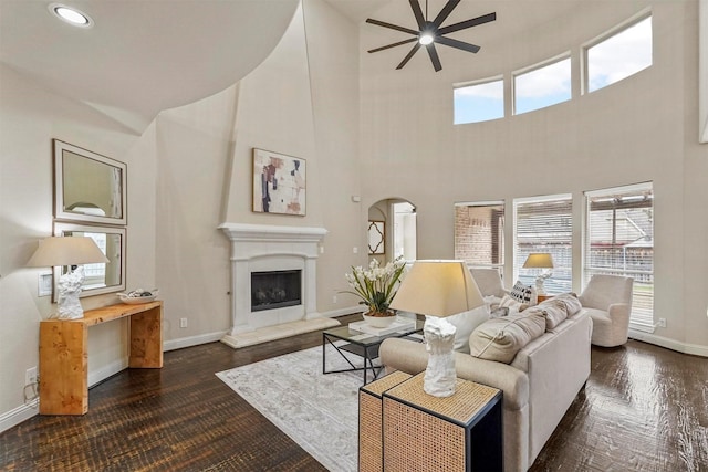 living room with ceiling fan, a high ceiling, and dark wood-type flooring