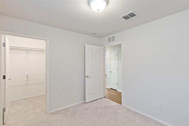 unfurnished bedroom featuring a closet, a walk in closet, and light carpet