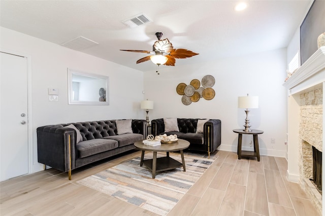 living room featuring ceiling fan and a stone fireplace