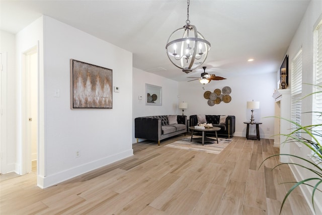 living room with light wood-type flooring and ceiling fan with notable chandelier