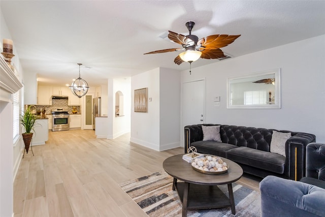 living room featuring light wood-type flooring, ceiling fan with notable chandelier, and a healthy amount of sunlight