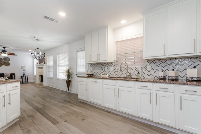 kitchen with a fireplace, decorative backsplash, white cabinets, sink, and pendant lighting