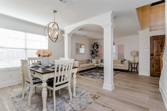 dining room with crown molding, decorative columns, light hardwood / wood-style flooring, and a chandelier