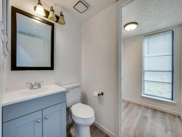 bathroom featuring wood-type flooring, toilet, vanity, and a textured ceiling