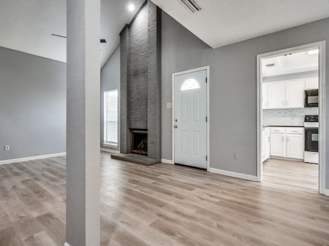 foyer entrance featuring a fireplace, light wood-type flooring, and high vaulted ceiling