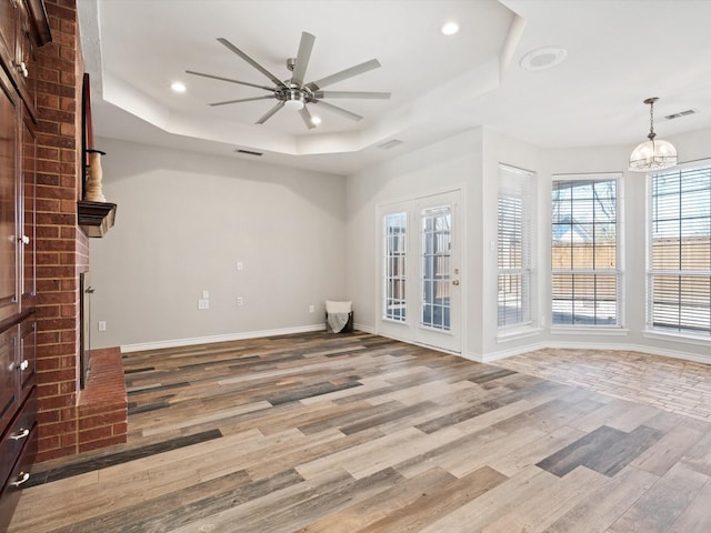 unfurnished living room with a raised ceiling, ceiling fan with notable chandelier, and light hardwood / wood-style floors