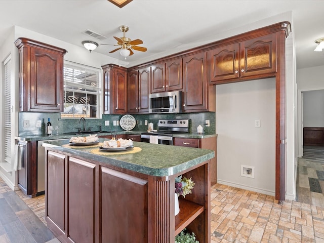 kitchen with sink, ceiling fan, appliances with stainless steel finishes, a kitchen island, and decorative backsplash