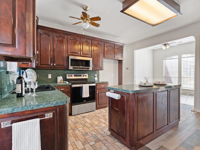 kitchen featuring ceiling fan, appliances with stainless steel finishes, decorative columns, a center island, and decorative backsplash