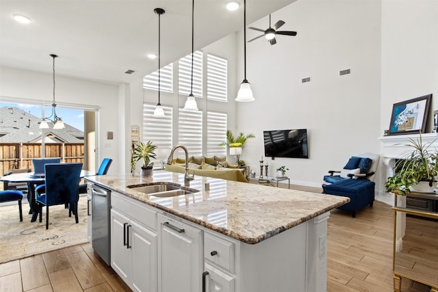 kitchen with sink, decorative light fixtures, white cabinetry, light stone countertops, and an island with sink