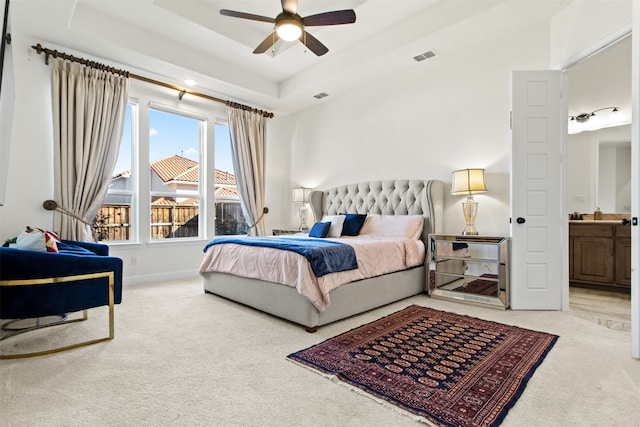 bedroom with ceiling fan, connected bathroom, carpet flooring, and a tray ceiling