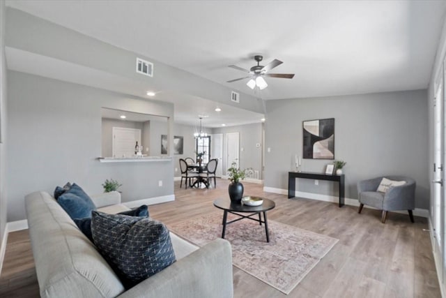 living room with ceiling fan with notable chandelier, lofted ceiling, and light wood-type flooring