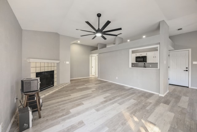 unfurnished living room featuring a tiled fireplace, light hardwood / wood-style floors, vaulted ceiling, and ceiling fan