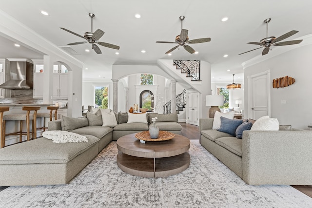 living room featuring ceiling fan, wood-type flooring, crown molding, and ornate columns