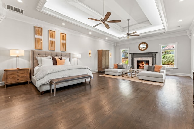 bedroom featuring ceiling fan, a tray ceiling, a premium fireplace, dark hardwood / wood-style floors, and ornamental molding