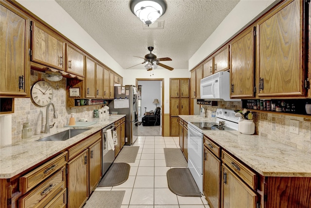 kitchen featuring light tile patterned floors, ceiling fan, a sink, appliances with stainless steel finishes, and brown cabinets