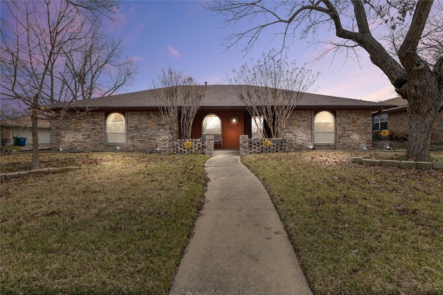 ranch-style house featuring a lawn, roof with shingles, and brick siding