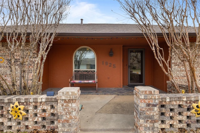 entrance to property with a porch, roof with shingles, and stucco siding