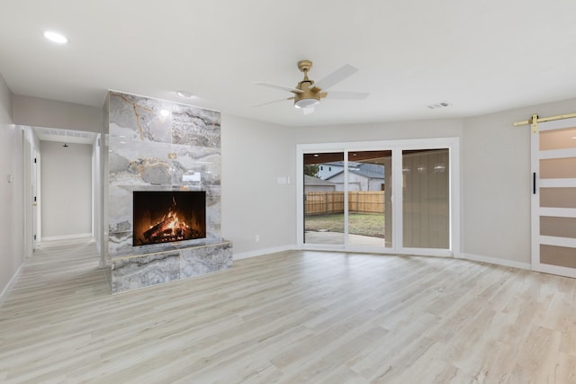 unfurnished living room with ceiling fan, light hardwood / wood-style flooring, a stone fireplace, and a barn door