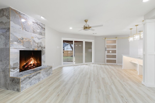 unfurnished living room with ceiling fan, a tile fireplace, a barn door, and light wood-type flooring