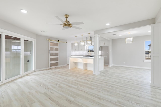 unfurnished living room featuring ceiling fan, light hardwood / wood-style flooring, and a barn door