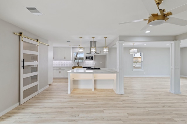 kitchen featuring stainless steel microwave, tasteful backsplash, white cabinetry, a barn door, and hanging light fixtures