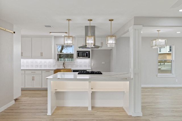 kitchen with hanging light fixtures, island range hood, stainless steel microwave, and white cabinetry