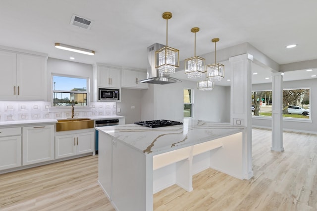 kitchen featuring light stone countertops, white cabinetry, stainless steel appliances, sink, and island range hood