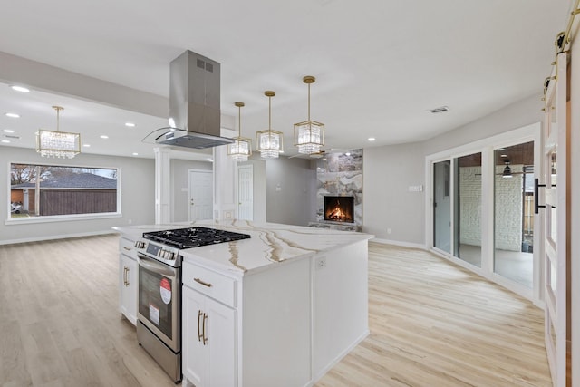 kitchen with stainless steel gas range oven, decorative light fixtures, island exhaust hood, and white cabinets