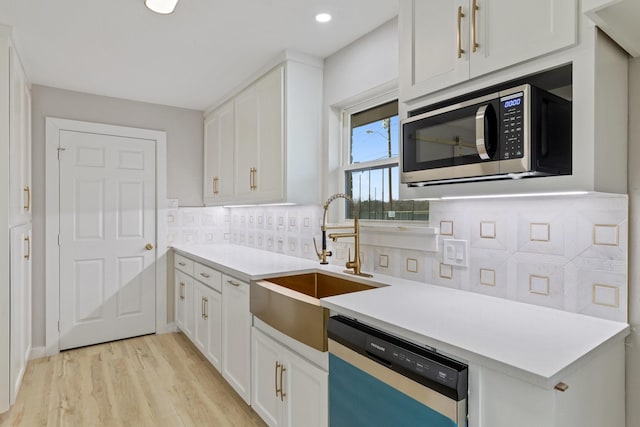 kitchen featuring sink, backsplash, white cabinets, light wood-type flooring, and stainless steel appliances