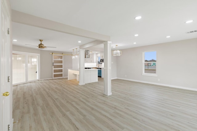 unfurnished living room featuring light wood-type flooring, ceiling fan with notable chandelier, and a barn door