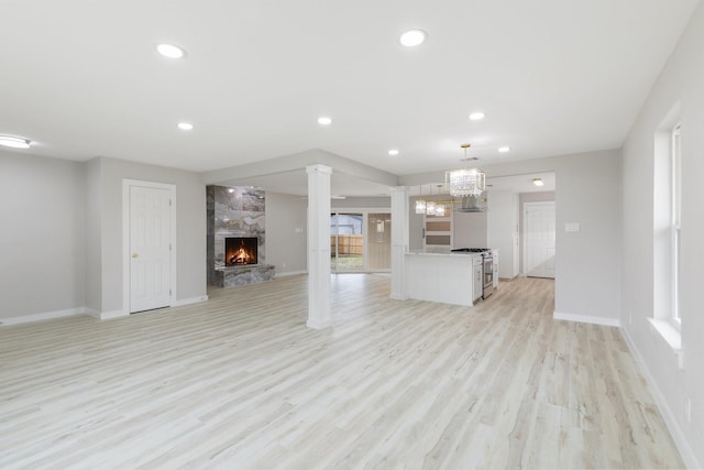 unfurnished living room with a large fireplace, a chandelier, ornate columns, and light hardwood / wood-style floors