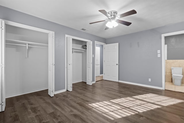 unfurnished bedroom featuring dark hardwood / wood-style flooring, ensuite bath, ceiling fan, and two closets