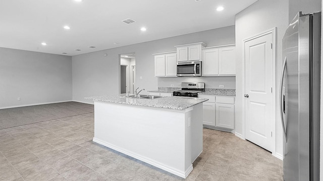 kitchen featuring light stone countertops, white cabinets, stainless steel appliances, sink, and a kitchen island with sink