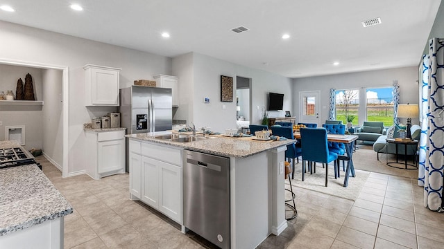 kitchen with white cabinetry, stainless steel appliances, sink, a kitchen island with sink, and light stone counters