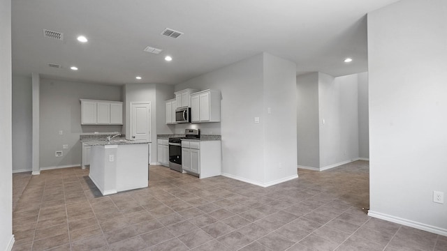 kitchen featuring light stone countertops, light tile patterned floors, white cabinets, stainless steel appliances, and a center island with sink