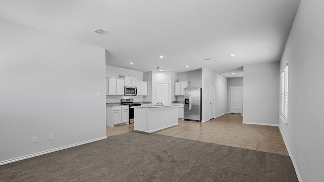 kitchen with appliances with stainless steel finishes, white cabinetry, light tile patterned floors, sink, and an island with sink