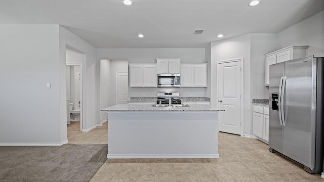 kitchen with light stone counters, white cabinetry, appliances with stainless steel finishes, and an island with sink