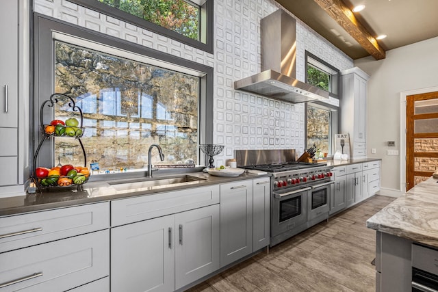 kitchen featuring sink, beam ceiling, double oven range, wall chimney exhaust hood, and gray cabinets