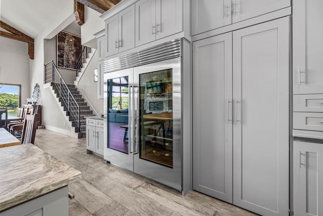 kitchen with light stone counters, wine cooler, and lofted ceiling with beams