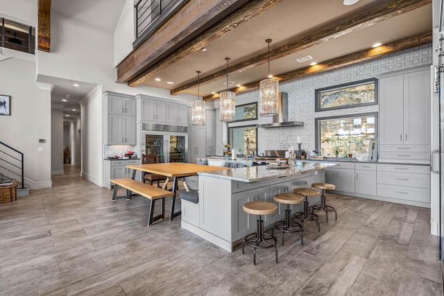 kitchen with pendant lighting, wall chimney range hood, light stone counters, a breakfast bar, and gray cabinetry