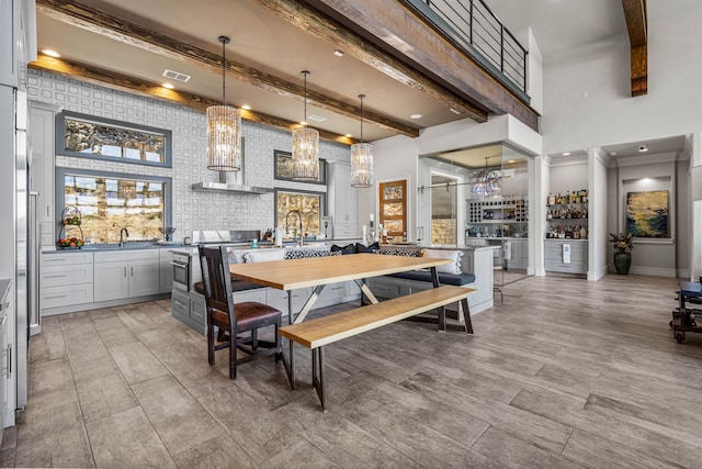 kitchen featuring hanging light fixtures, gray cabinetry, a breakfast bar, wall chimney range hood, and beamed ceiling