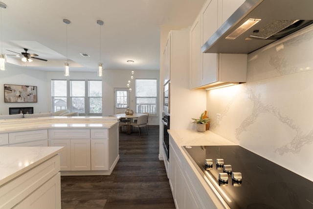 kitchen with white cabinets, black appliances, wall chimney exhaust hood, dark wood-type flooring, and hanging light fixtures