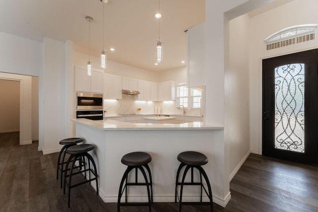 kitchen featuring white cabinets, decorative light fixtures, sink, kitchen peninsula, and a breakfast bar