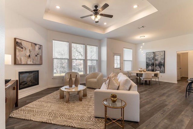 living room with dark wood-type flooring, ceiling fan, and a raised ceiling