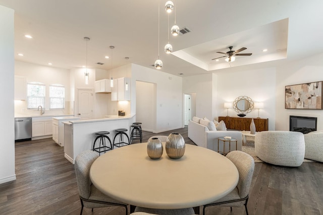 dining room featuring ceiling fan, sink, a tray ceiling, and dark hardwood / wood-style floors