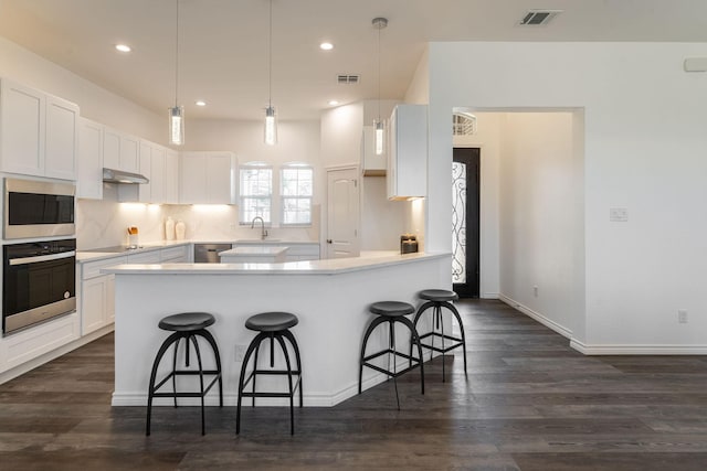 kitchen with white cabinets, stainless steel appliances, sink, a kitchen breakfast bar, and dark hardwood / wood-style floors