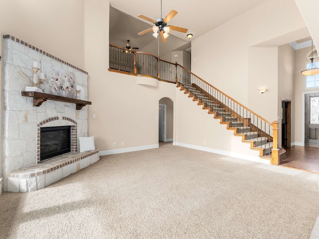 unfurnished living room with carpet floors, ceiling fan, a towering ceiling, and a fireplace